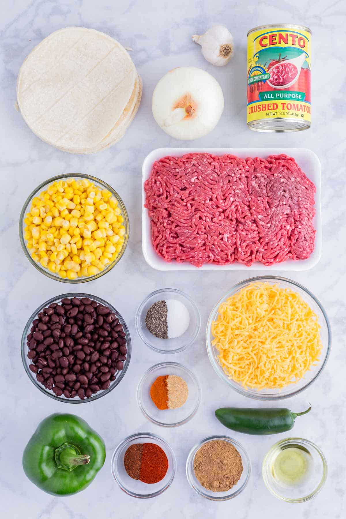 Ground beef, black beans, corn, cheese, corn tortillas, veggies, and taco seasoning are the main ingredients for this dish.