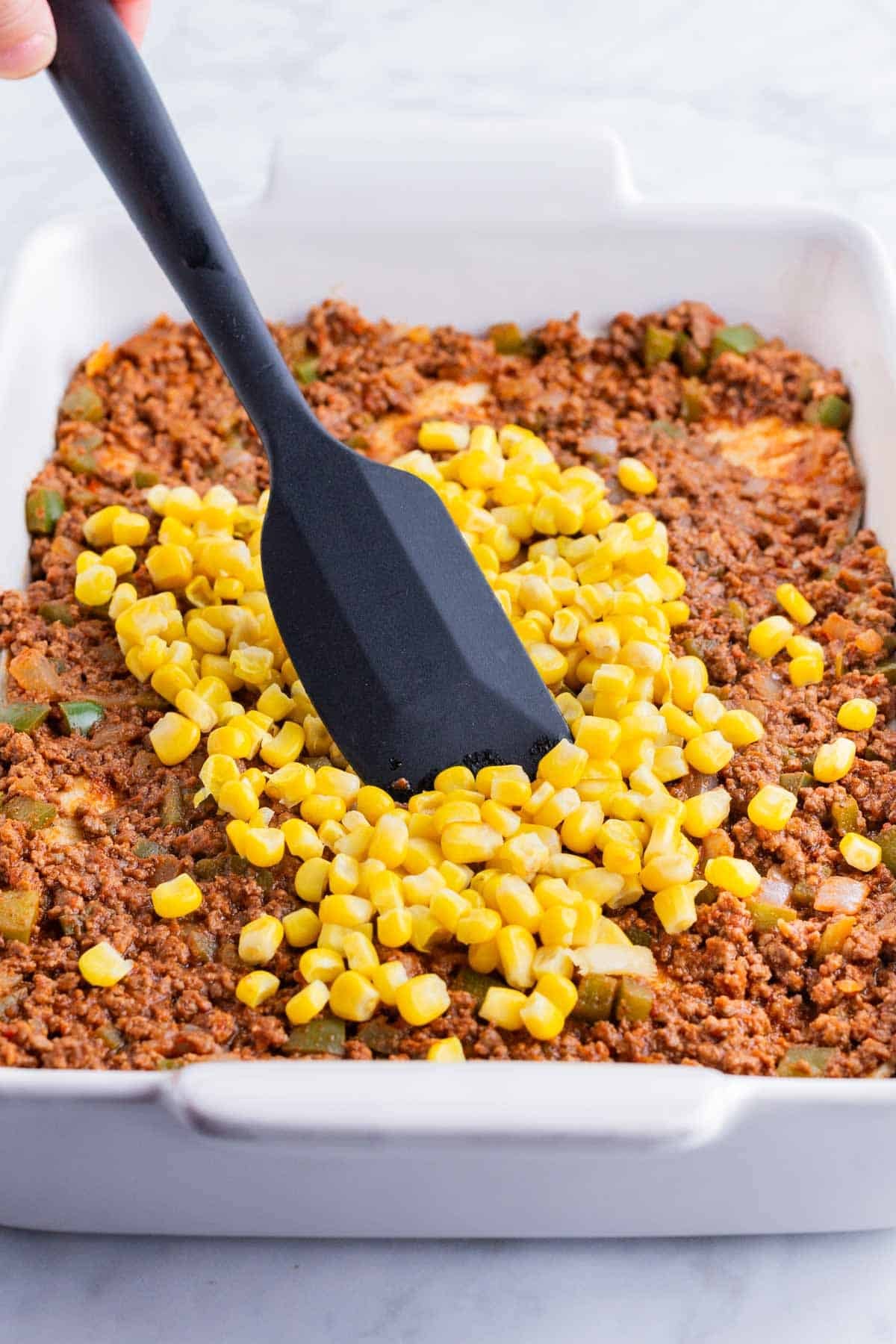 A spatula spreads corn while layering the taco lasagna.