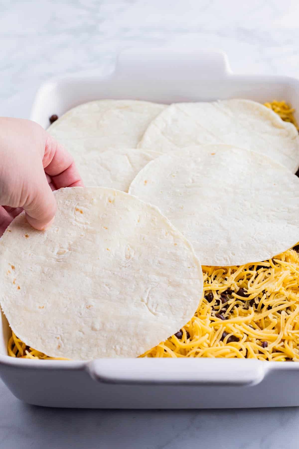 A hand places corn tortillas while layering the taco lasagna.