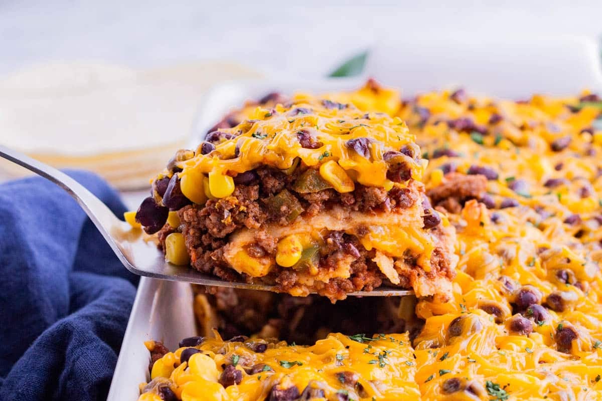 A spatula picks up a serving of Mexican lasagna from the baking dish.