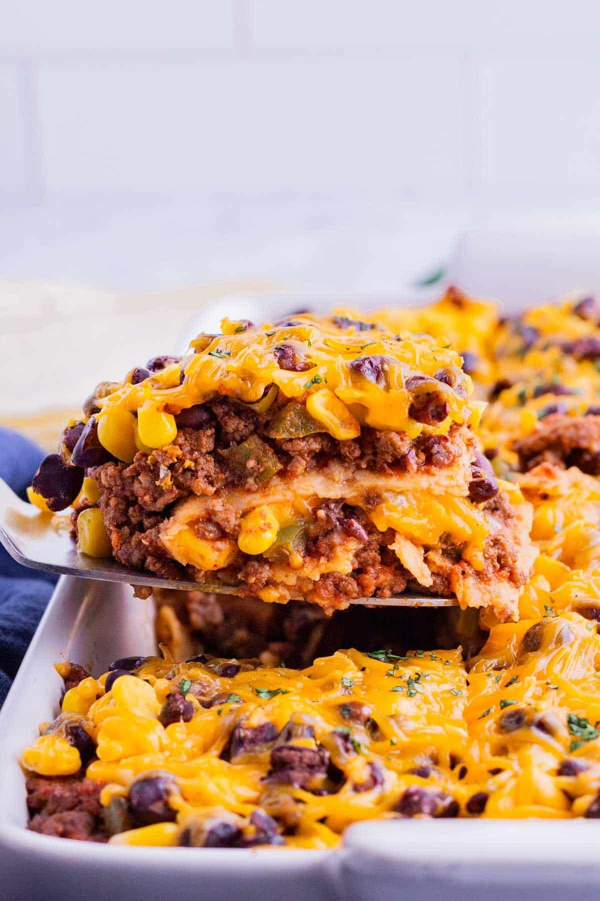 A spatula picks up a serving of Mexican lasagna from the baking dish.