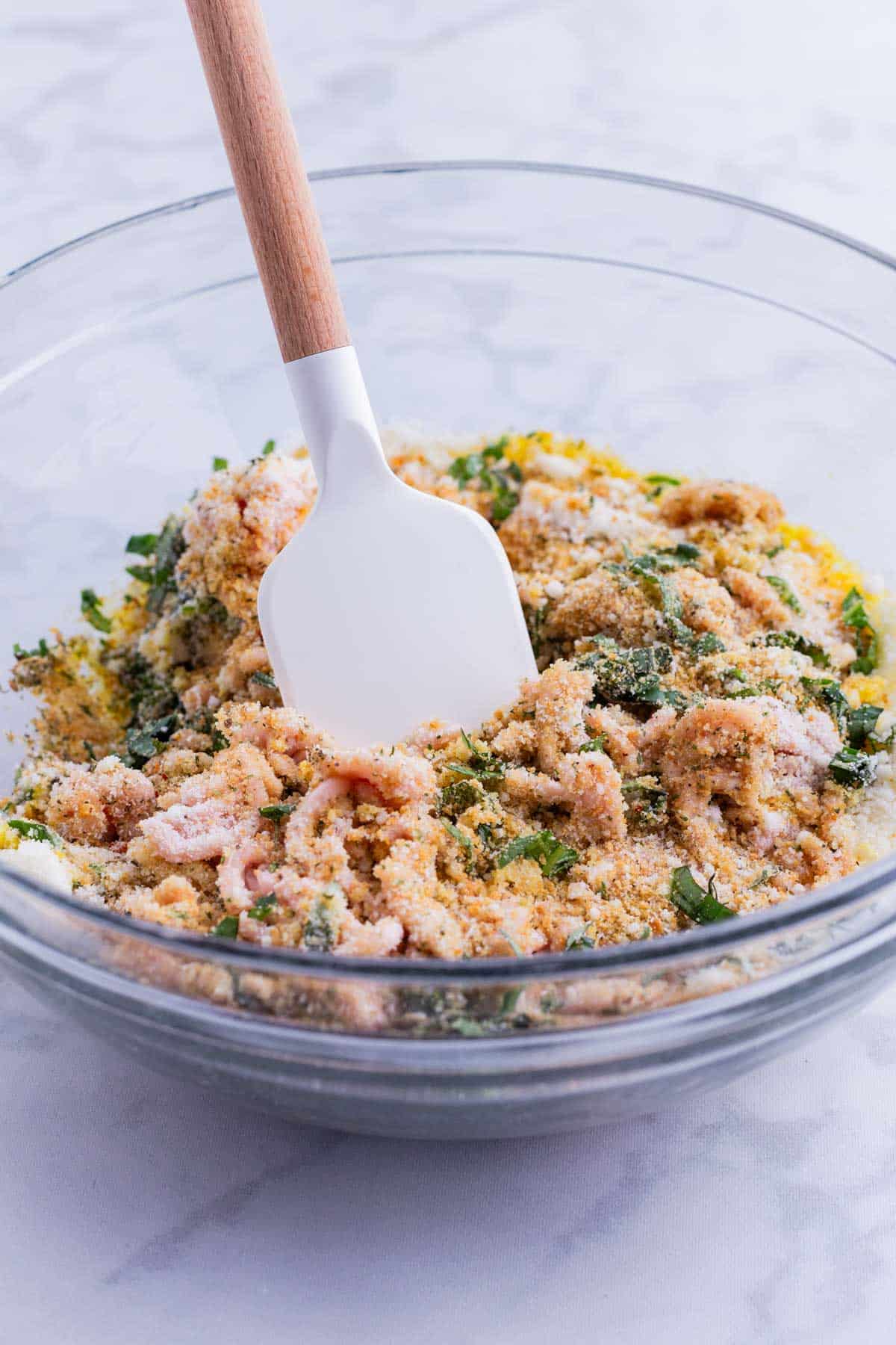 A spatula stirs a ground chicken mixture in a glass bowl.