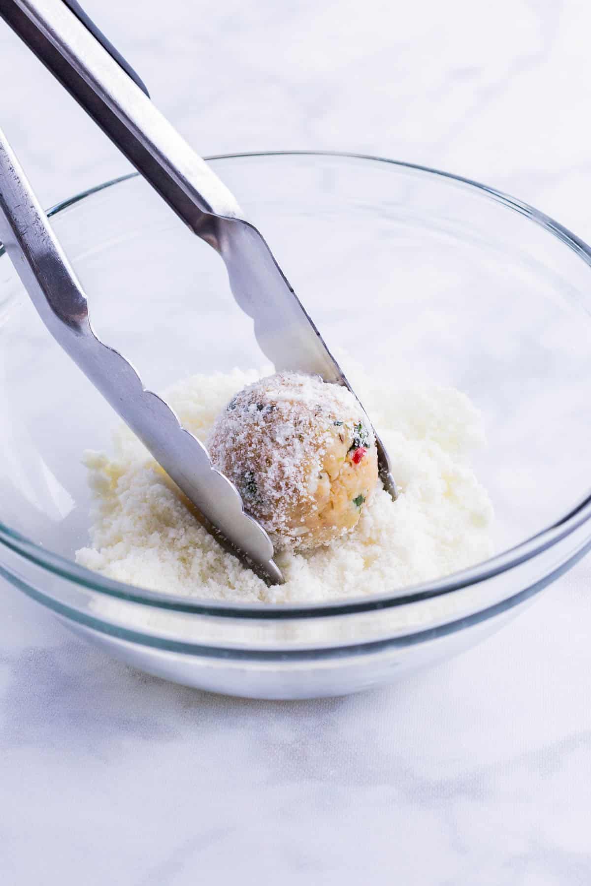 A chicken meatball is rolled in grated Parmesan cheese.