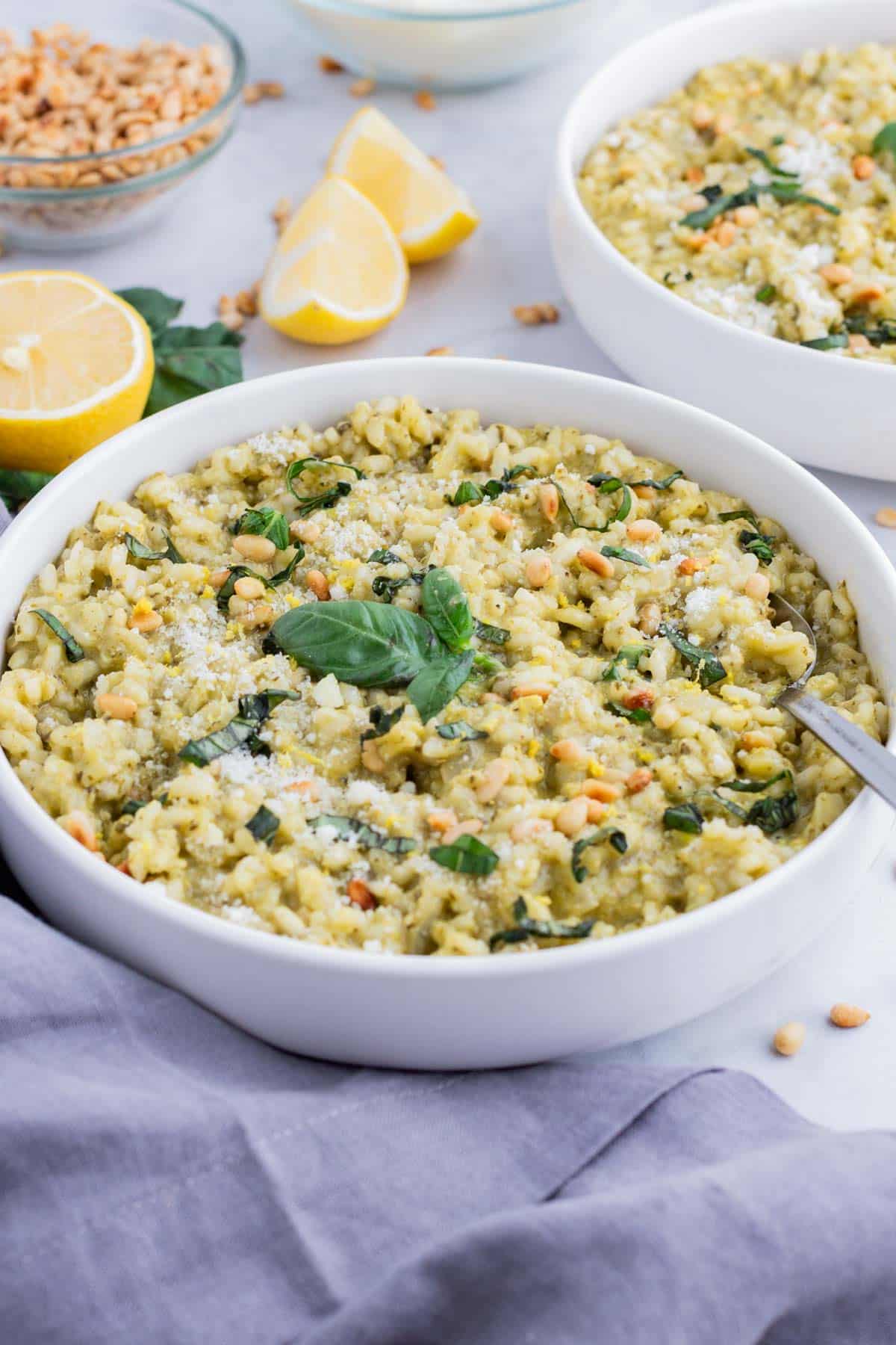 Pesto risotto is topped with fresh basil and served in a white bowl.