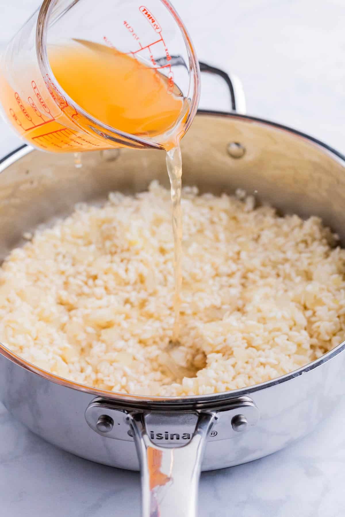 Broth is slowly added to the risotto in a pot.