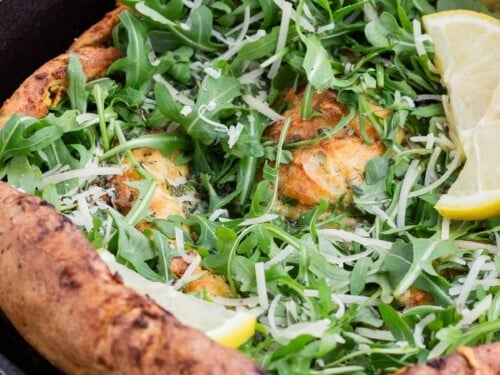 The toppings of arugula and parmesan cheese are added to the cooked Dutch baby.