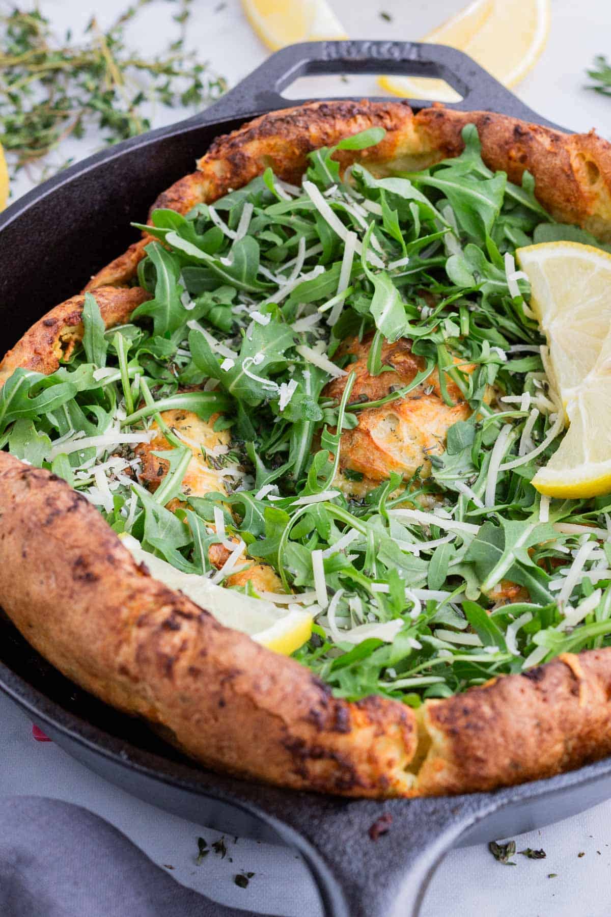 The toppings of arugula and parmesan cheese are added to the cooked Dutch baby.