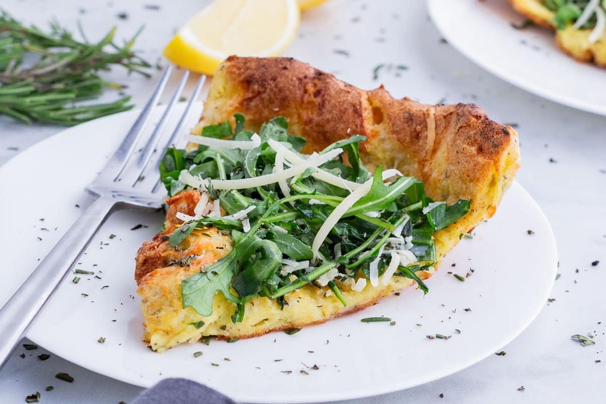 A slice of savory Dutch baby served on a white plate with arugula and lemon.