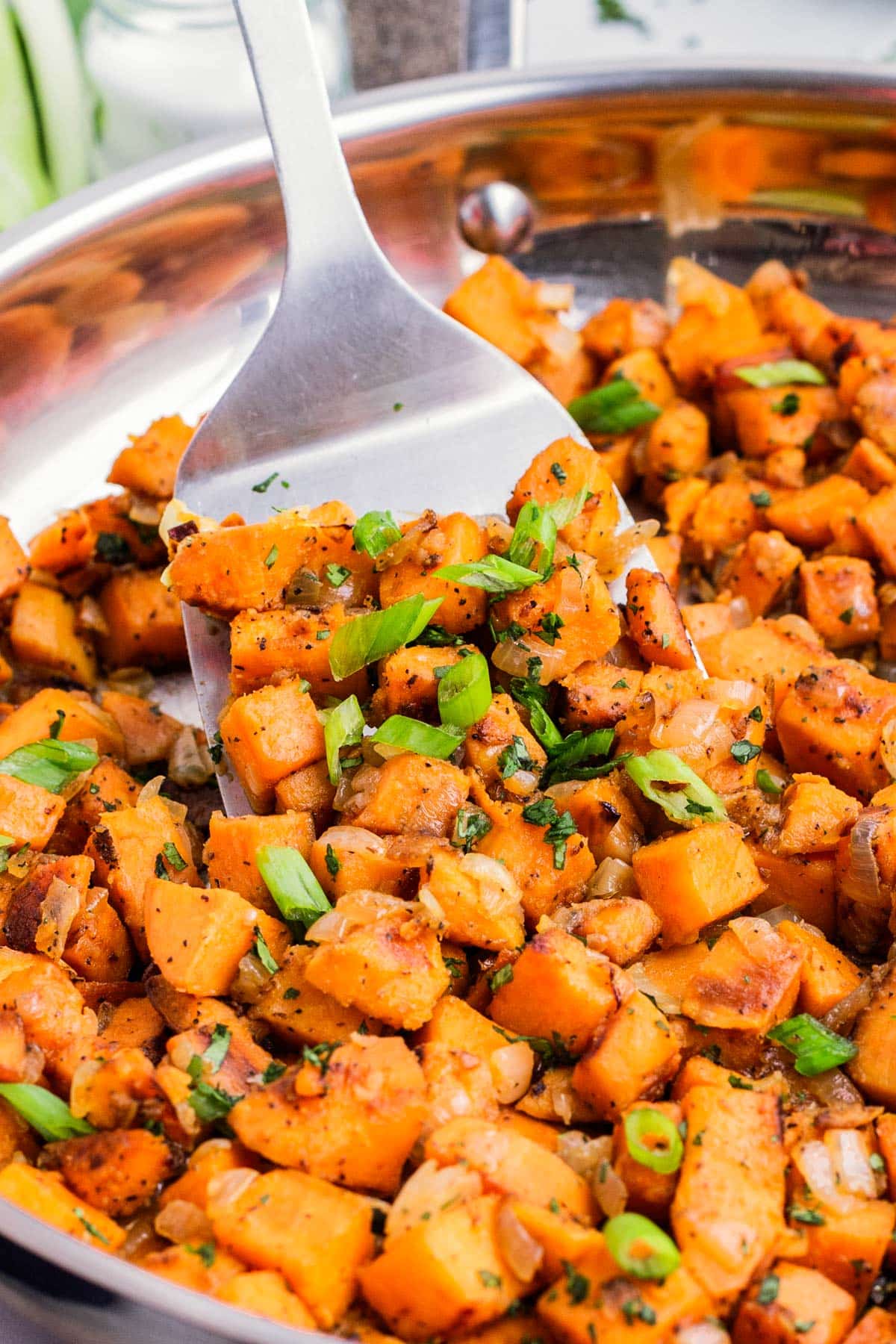 A spatula scoops up some Skillet Sweet Potatoes with cilantro and green onions.