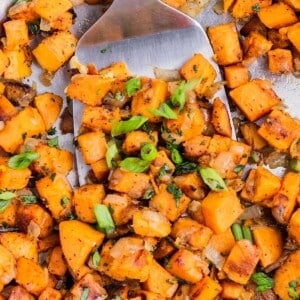 A metal spatula scoops up some diced sweet potatoes from a skillet.