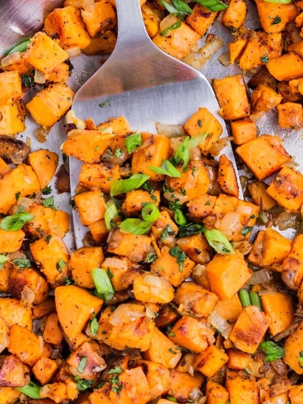 A metal spatula scoops up some diced sweet potatoes from a skillet.