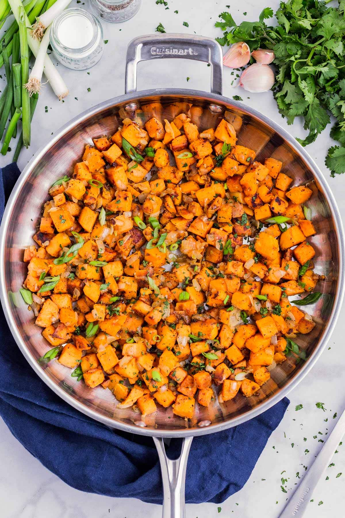 A stainless steel skillet is full of diced sweet potatoes after cooking.