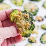 A hand holds a piece of broccoli roasted in the oven.