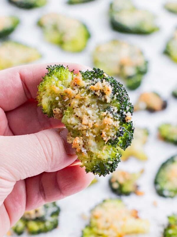 A hand holds a piece of broccoli roasted in the oven.