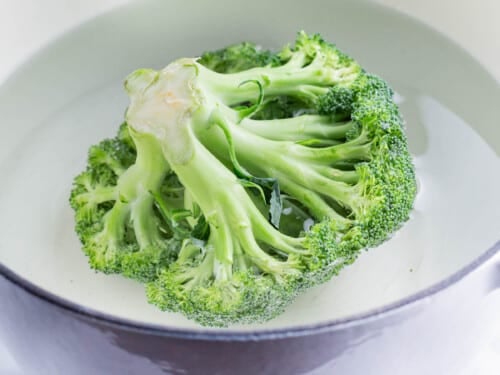 A head of broccoli is boiled in a pot of water.