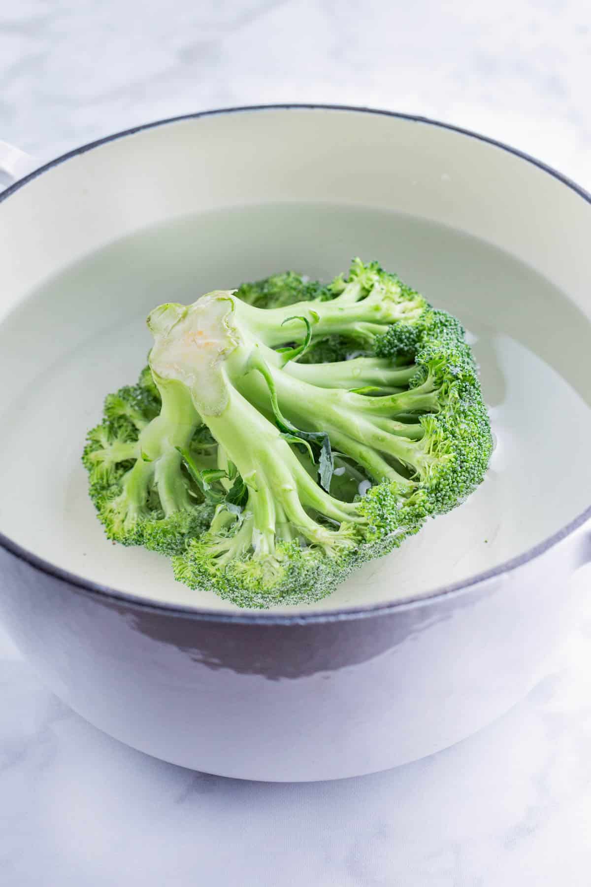 A head of broccoli is boiled in a pot of water.