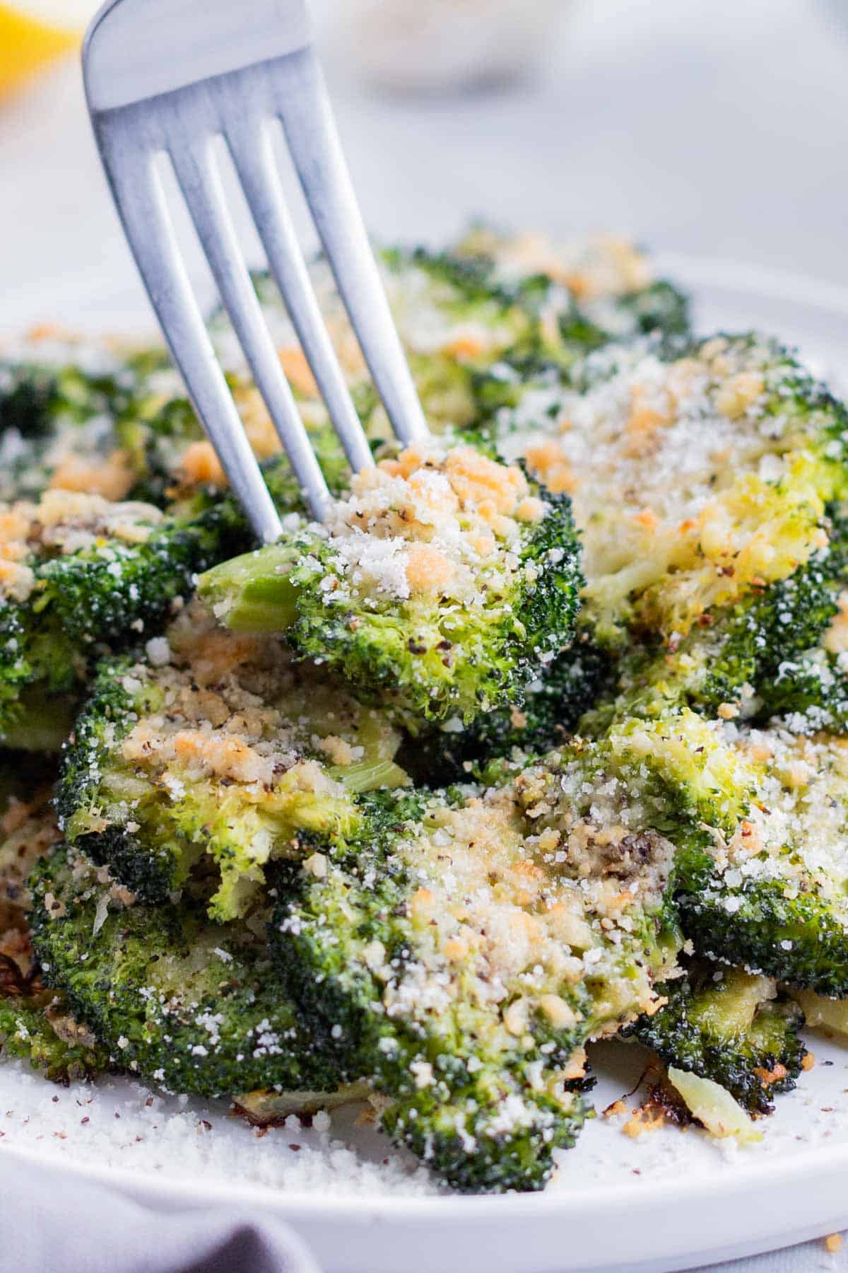 A fork digs into a bowl of crispy smashed broccoli.