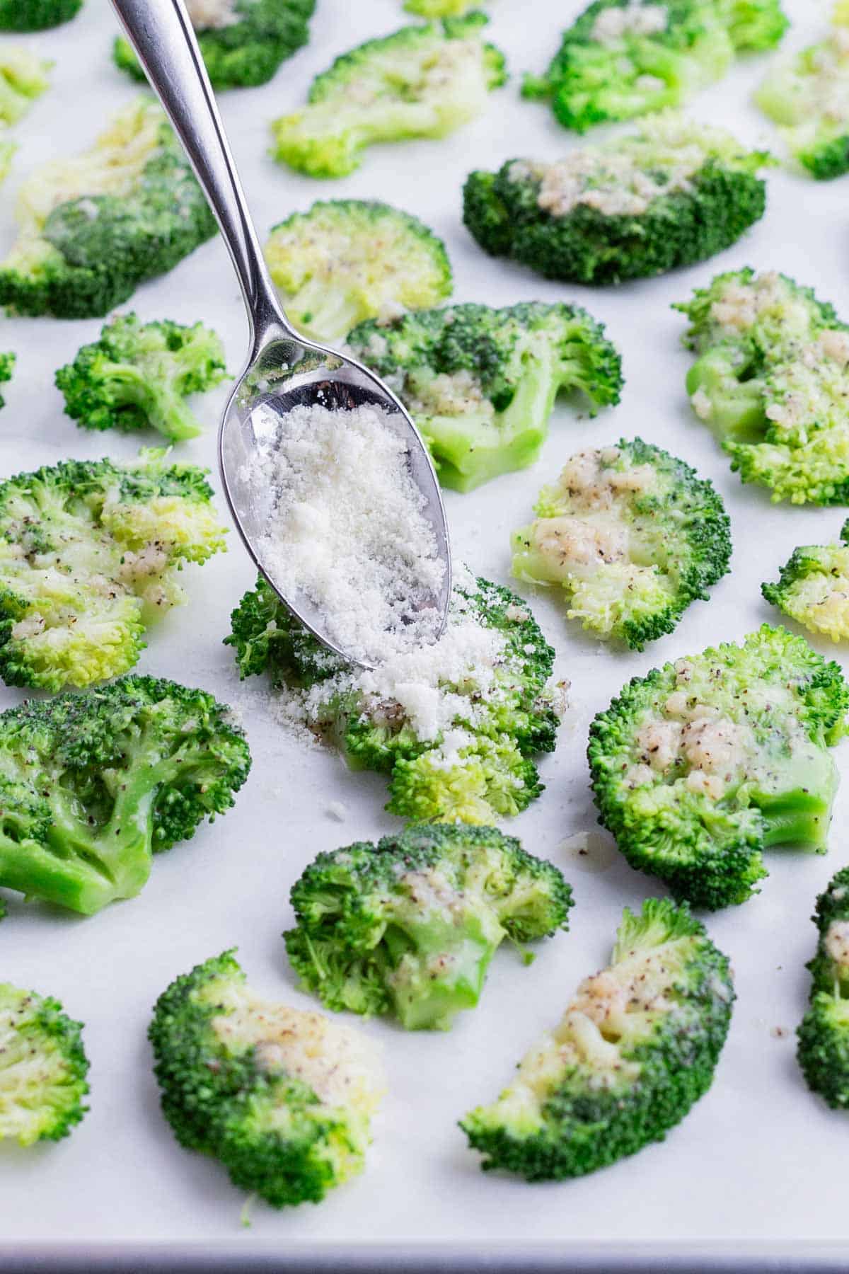 A spoon sprinkles cheese over the smashed broccoli.