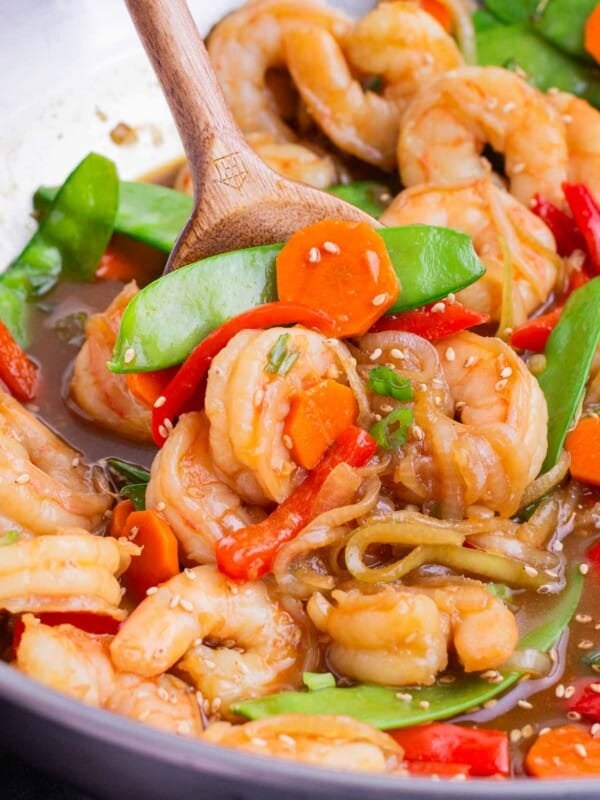 A wooden spoon stirs teriyaki shrimp stir fry in a wok.