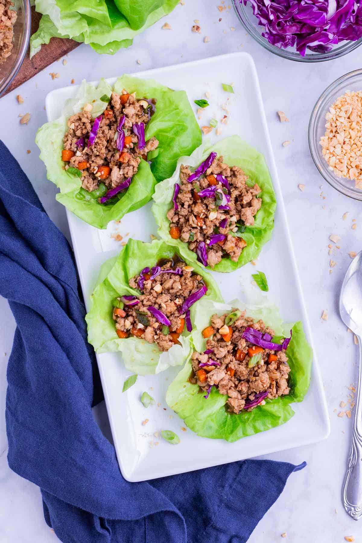 Four Thai chicken lettuce wraps are served on a white plate.