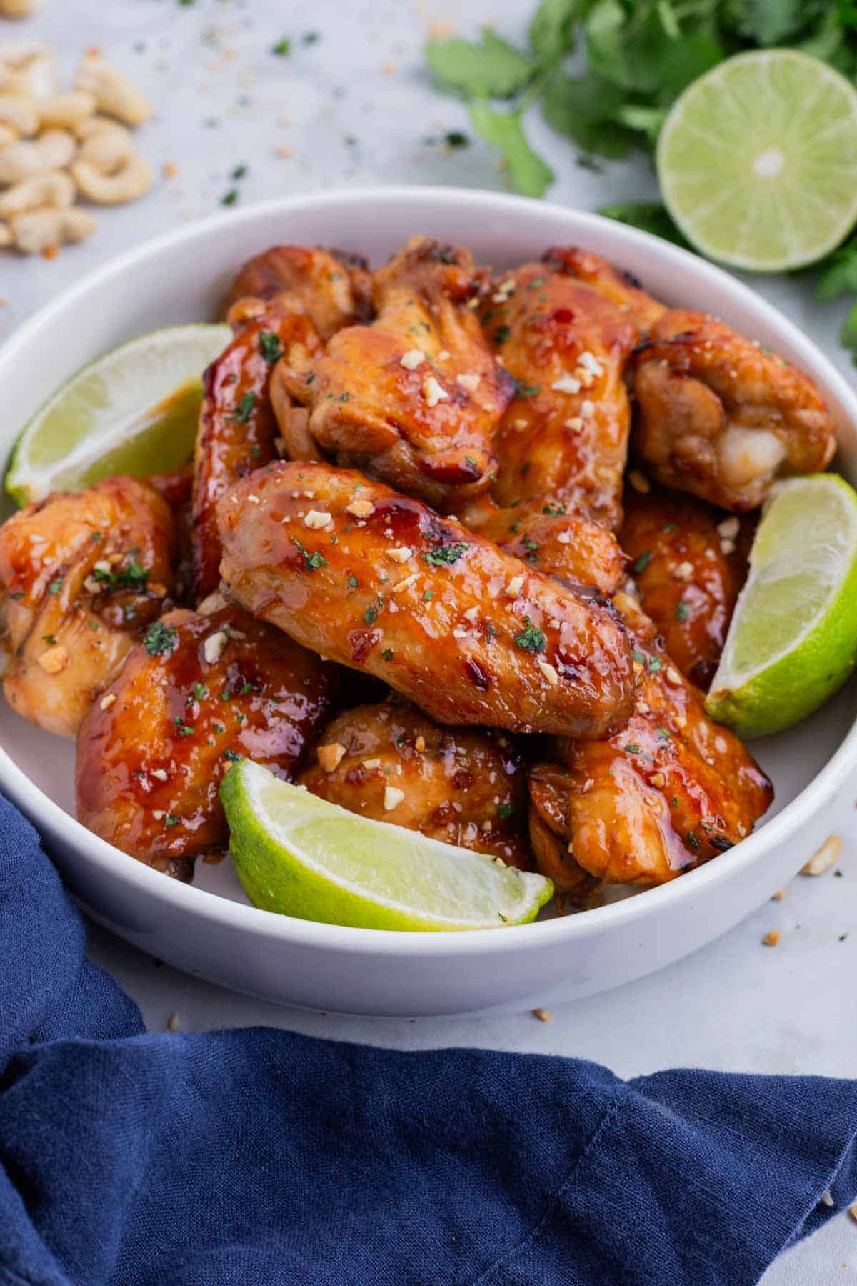 A bowl full of Thai chicken wings are served with lime wedges.