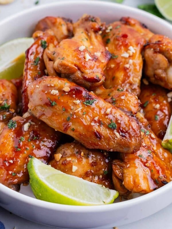 A bowl full of Thai chicken wings are served with lime wedges.