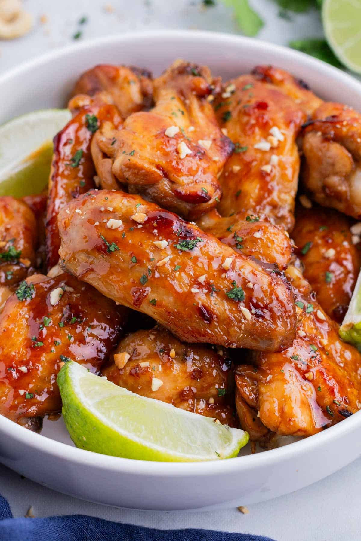 A bowl full of Thai chicken wings are served with lime wedges.