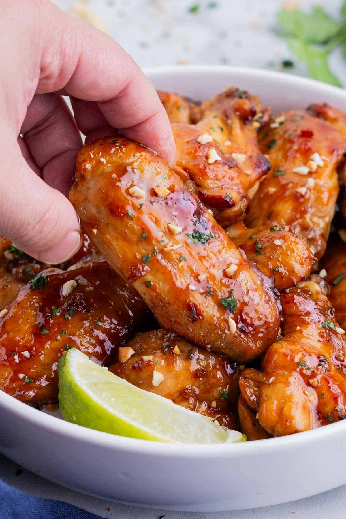 A hand picks up an Thai chicken wing from a white bowl.