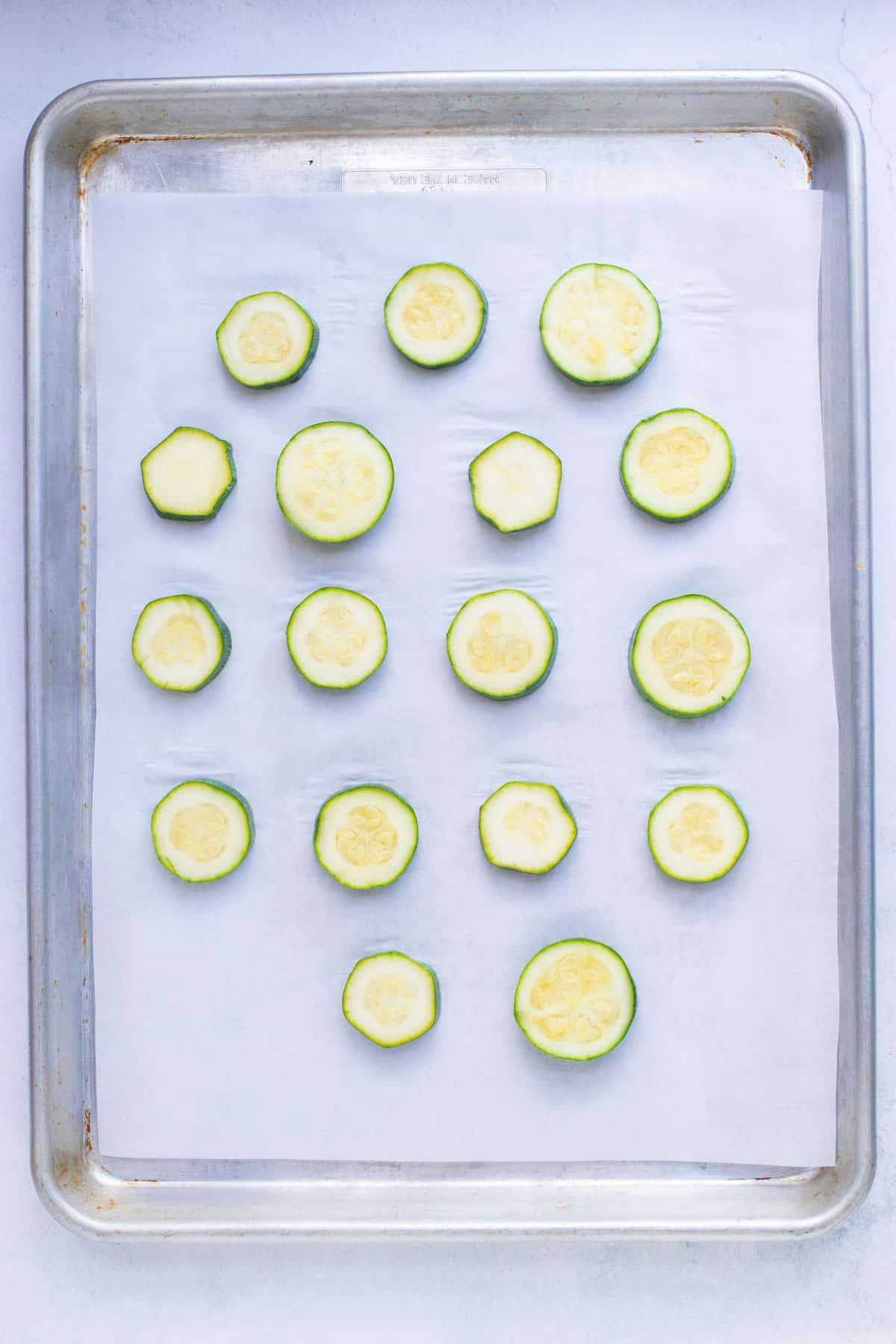 Instructional pictures for preparing zucchini to be frozen by putting them on a large baking sheet.