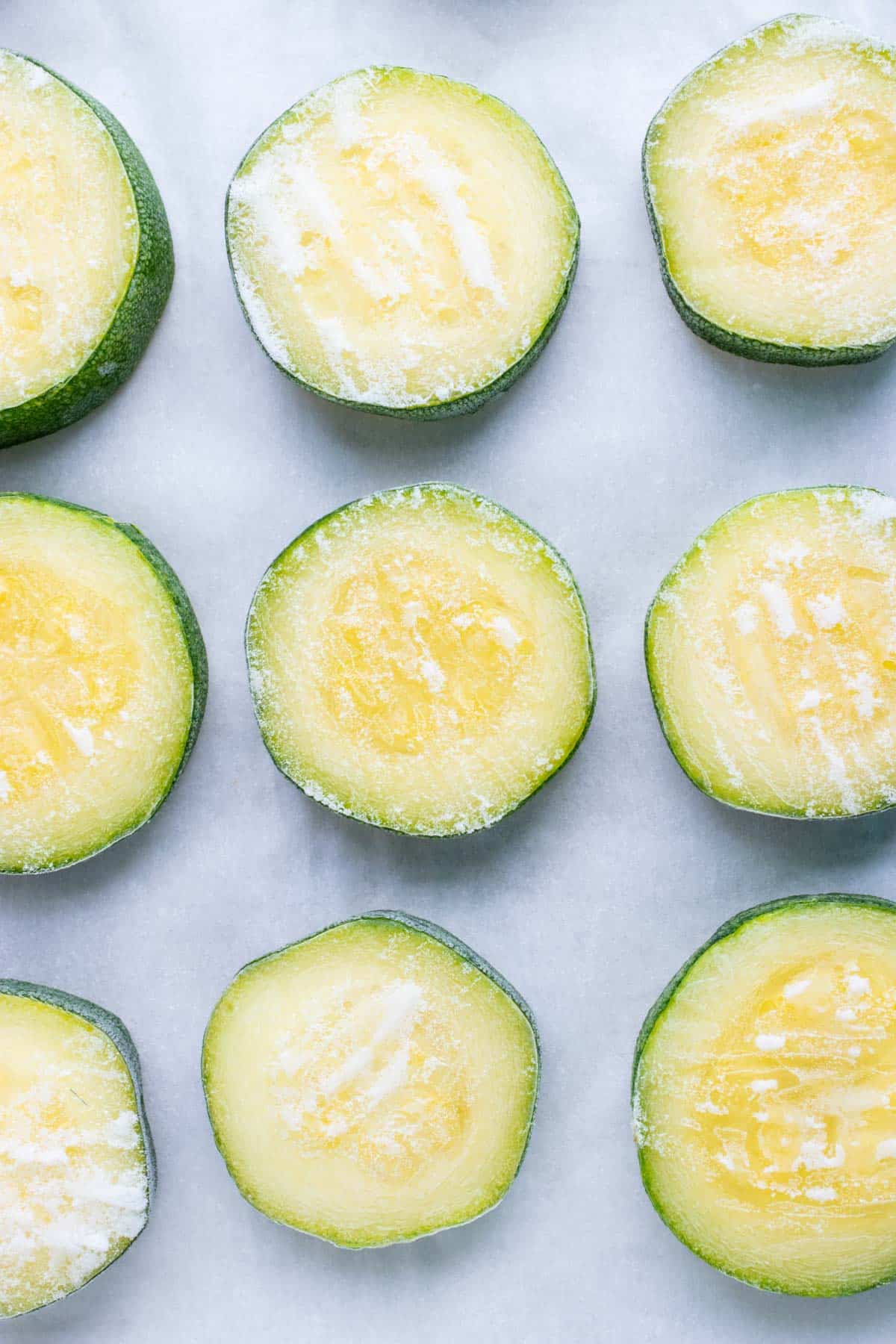 Zucchini slices are laid flat on a sheet pan to be frozen.