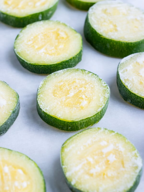 Summer squash in slices are put on a sheet pan with space between them.