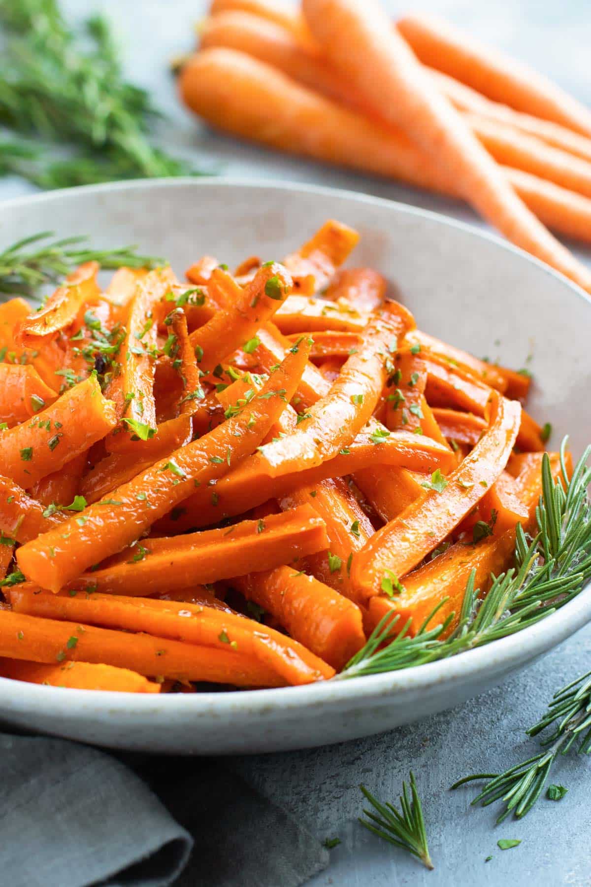 Side picture of roasted carrots in a white bowl with rosemary.