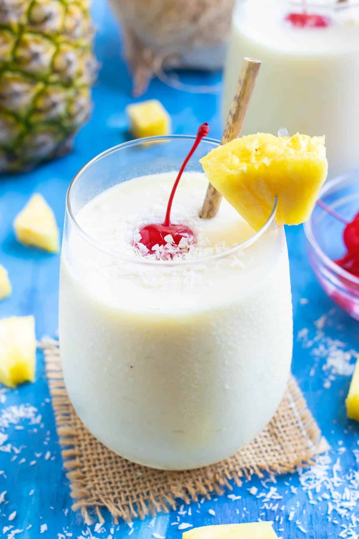 A frozen pina colada recipe in a clear glass with a pineapple wedge and a maraschino cherry.
