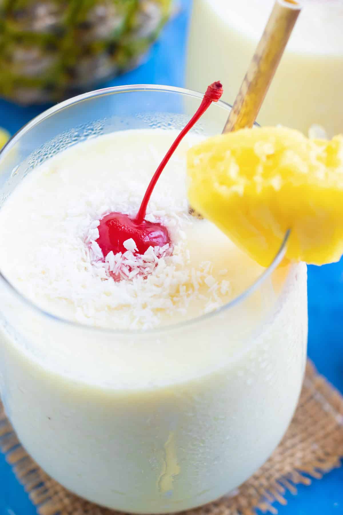 A frozen pina colada recipe in a clear glass with a pineapple wedge and a maraschino cherry.