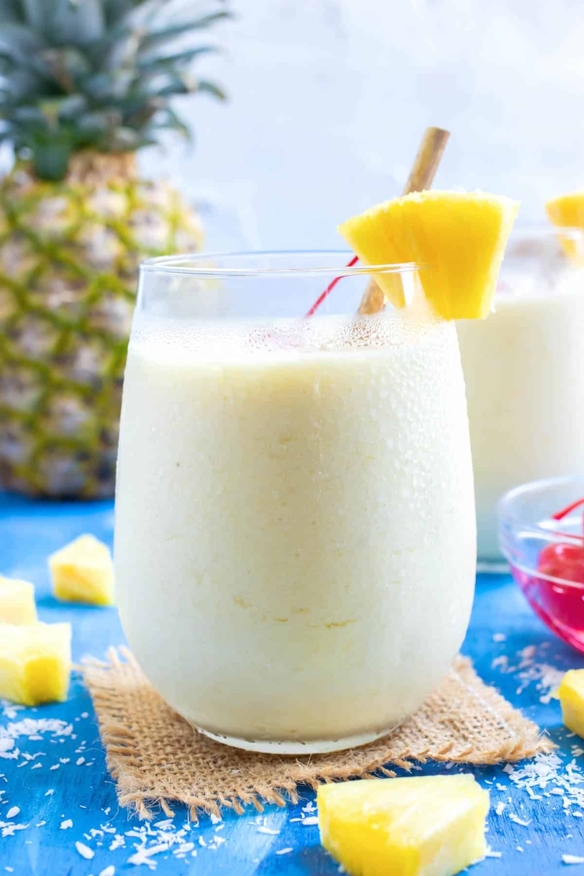 A glass full of a frozen pineapple cocktail recipe with a whole pineapple in the background.