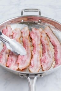 Bacon strips are cooked in a skillet.