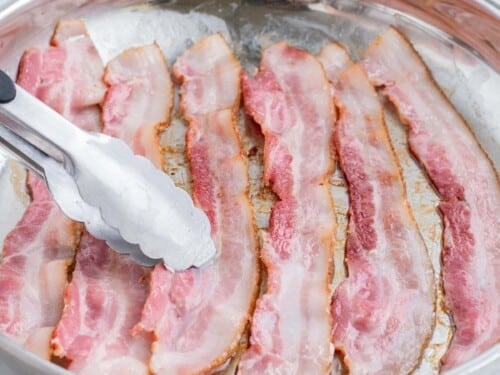 Bacon strips are cooked in a skillet.