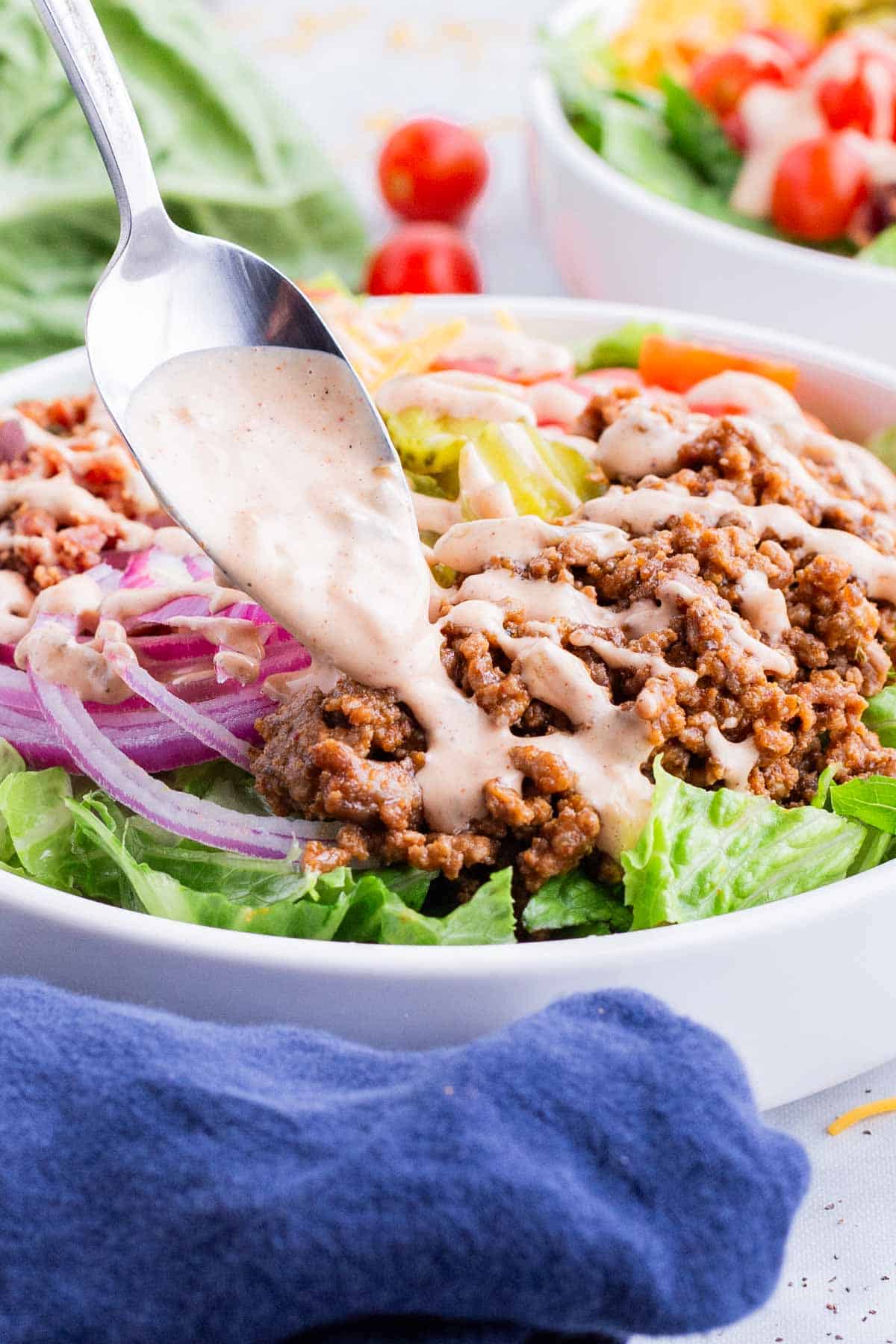 A spoon drizzles burger sauce over the bowl.