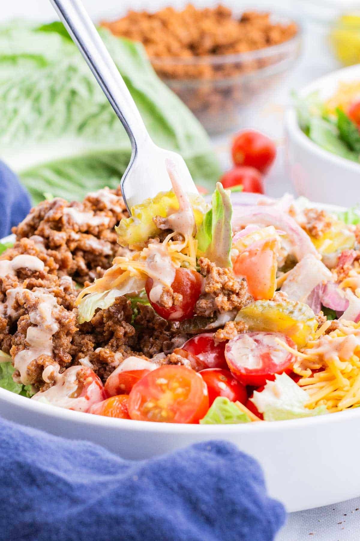 A fork digs into a big bowl full of deconstructed burger.