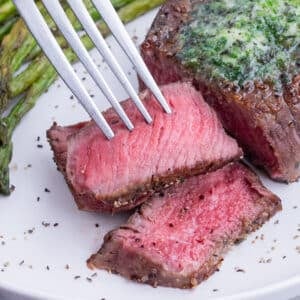 A medium-rare slice of filet mignon steak is being picked up with a fork.