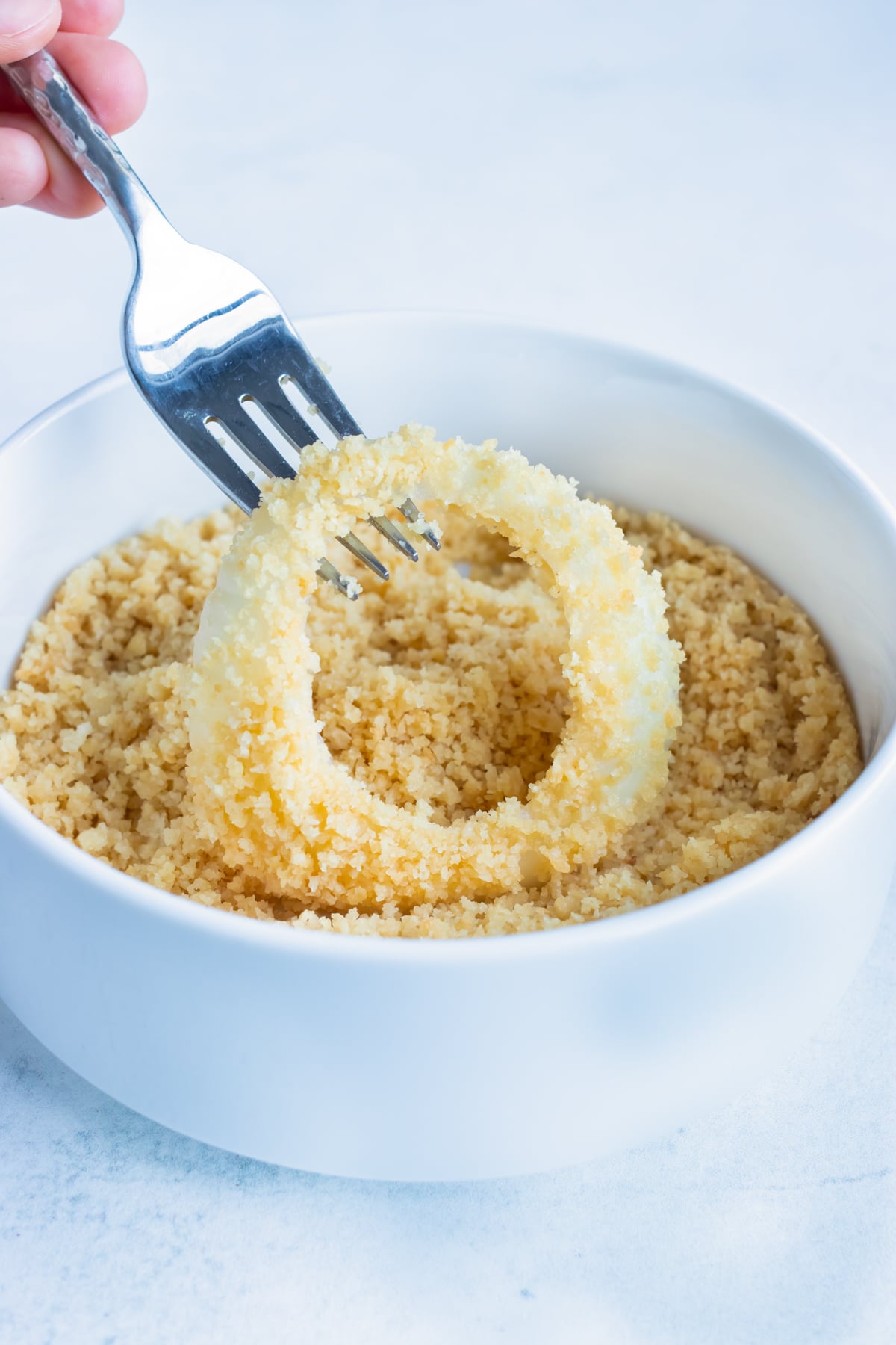 Pressing an onion ring into panko breadcrumbs to coat it before air frying.