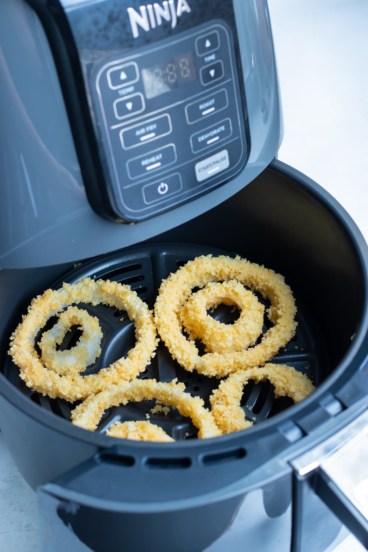 Breaded onion rings in a single layer in the air fryer basket, with smaller rings nested inside bigger ones.