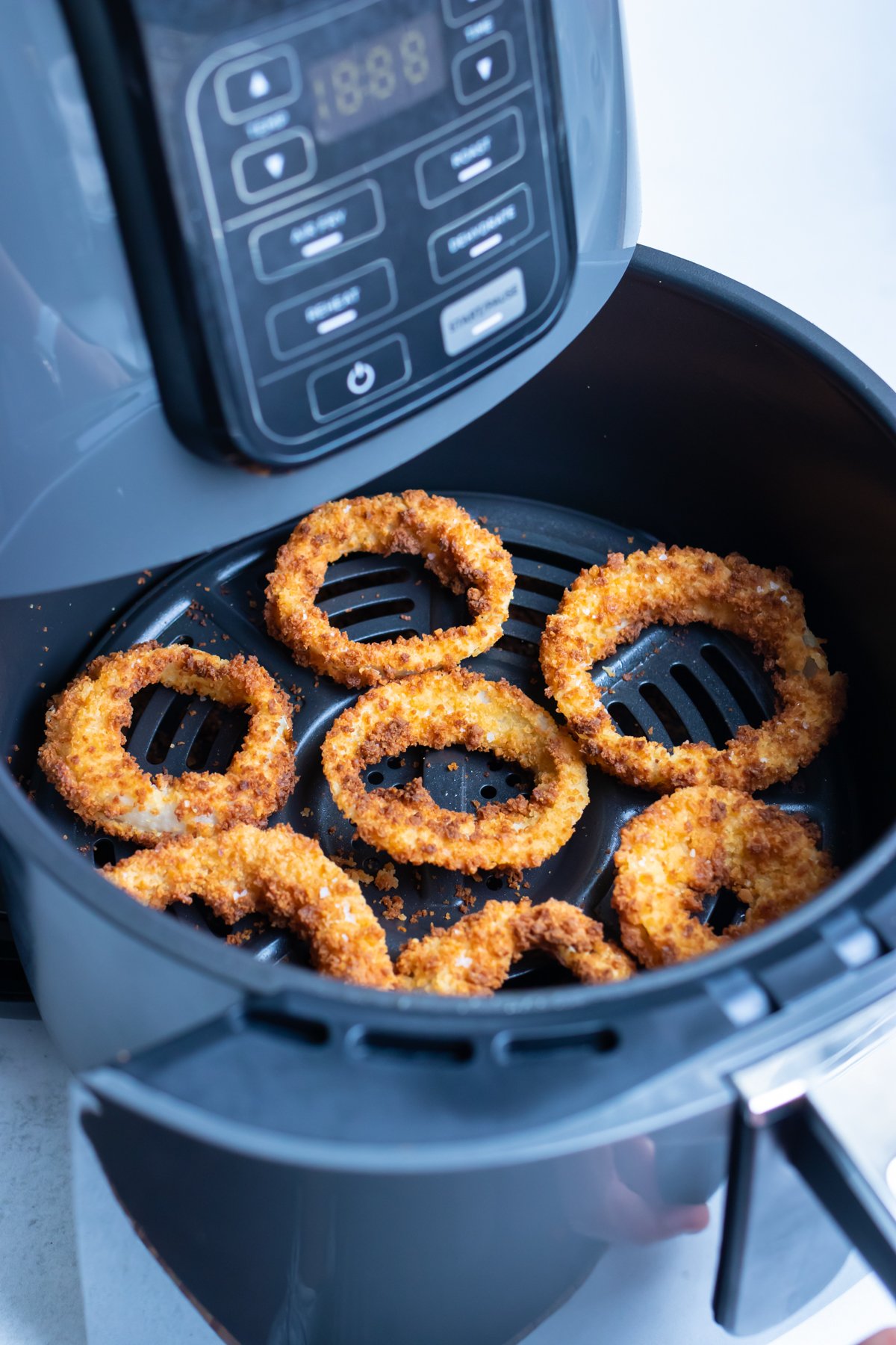 A layer of golden, crispy onion rings are shown in the air fryer.