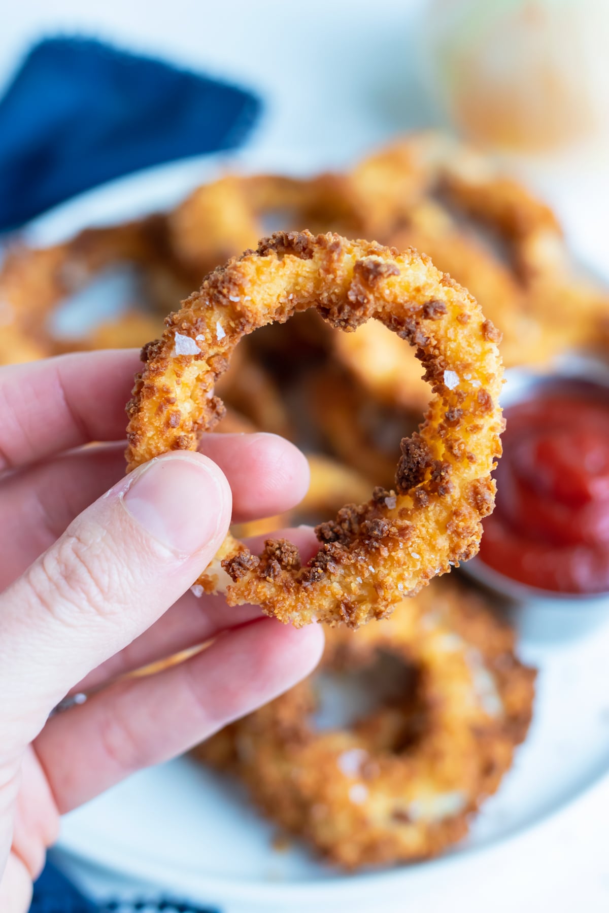 Hand holding a crispy homemade air fryer onion ring with a golden panko crust.