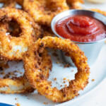 Ultra crispy onion rings are served as an appetizer on a white plate.