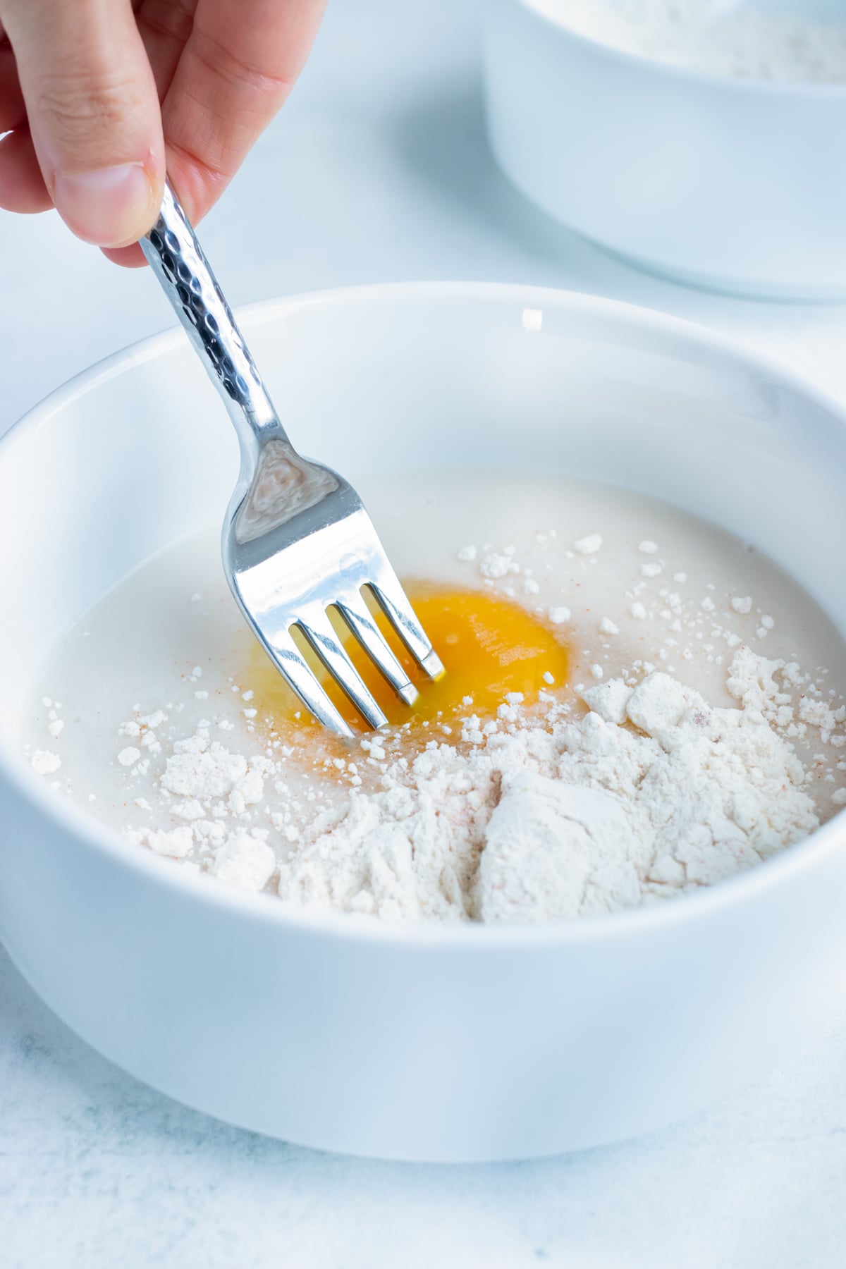 Whisking seasoned flour into the egg wash to make a thick batter for onion rings.
