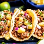 A middle taco in a row of tacos al pastor with pineapple and chipotle.