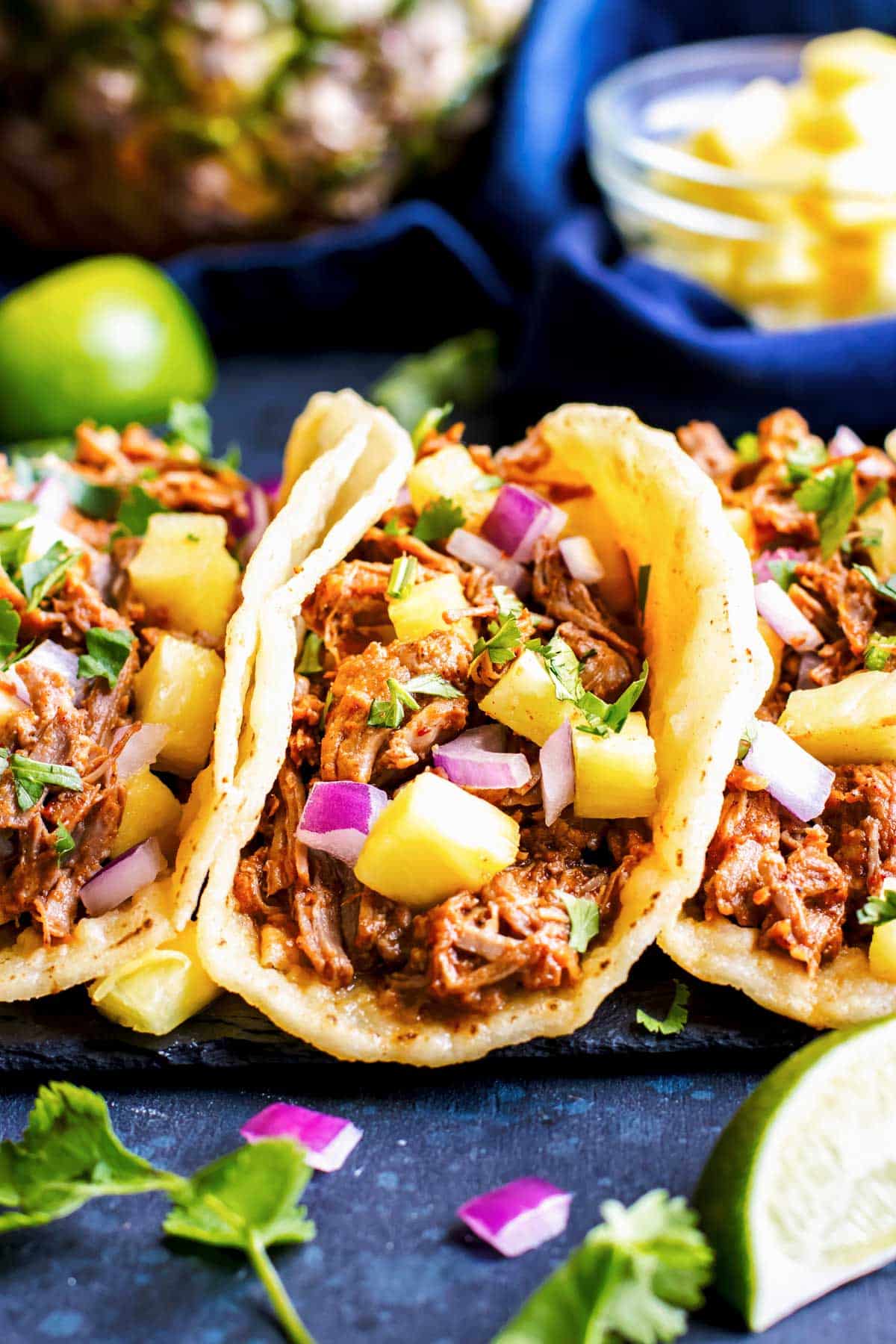 Instant Pot Tacos al Pastor RECIPE with three tacos lines up and topped with red onion and pineapple