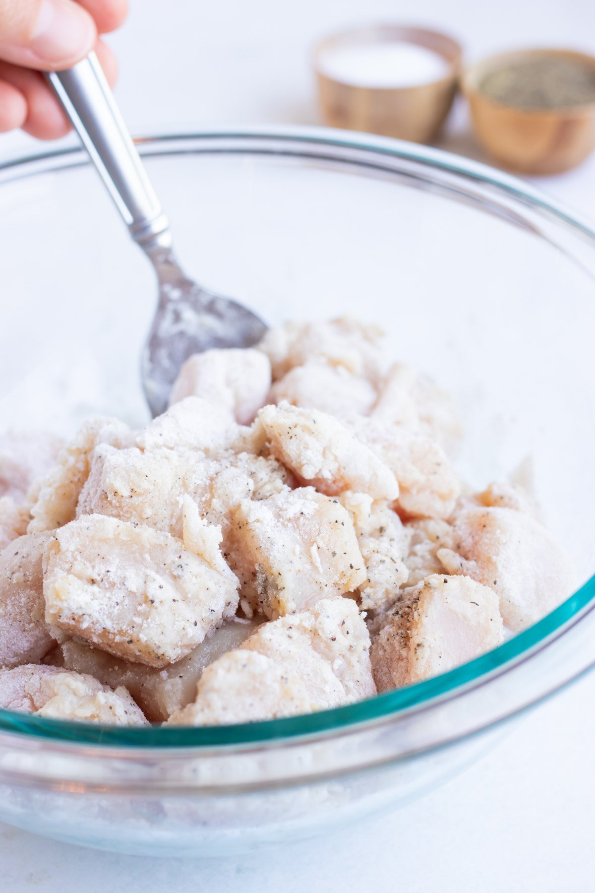 Chicken cubes being tossed in a flour mixture.
