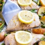 A metal spatula picking up a baked chicken breast with a lemon slice from a baking pan.